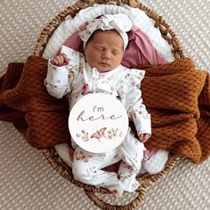 a baby is sleeping in a basket holding a sign that says i'm here