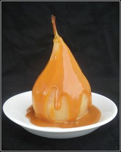 a pear covered in caramel sauce sitting on a white plate against a black background