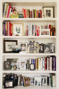 a white book shelf filled with lots of books and framed pictures on top of it