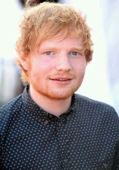 a man with red hair and blue eyes looks at the camera while wearing a black shirt