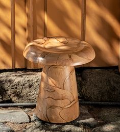 a wooden stool sitting on top of a stone floor next to a wall and tree