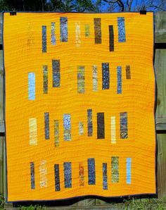 an orange quilt is hanging on a wooden fence in front of some grass and trees