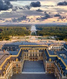 an aerial view of a large building in the middle of a field with trees and clouds