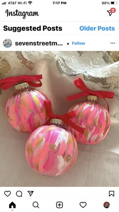 three pink and gold ornaments with red bows on them sitting on a white table cloth