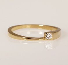 a yellow gold ring with a single diamond on the top, sitting on a white surface