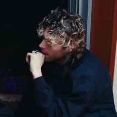 a man with curly hair sitting in front of a window