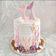 a white cake with pink and purple frosting on top, topped with two mermaid tail decorations