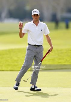 a man in white shirt and grey pants holding a golf club with his hand up