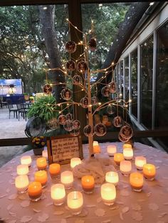 a table topped with lots of lit candles next to a tree filled with small ornaments