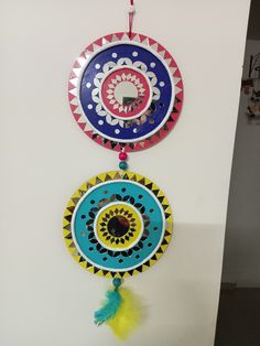 two colorful circular objects hanging on a wall next to each other, one with a yellow feather