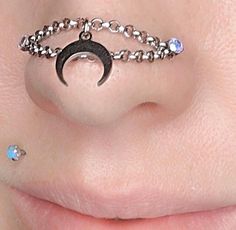 a woman's nose is adorned with silver chains and an upside down crescent piercing