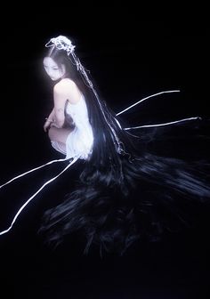 a woman with long black hair sitting on the ground in front of a dark background