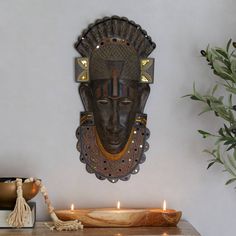 a wooden table topped with a vase filled with flowers next to a wall mounted mask