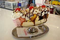 an ice cream sundae with bananas, cherries and whipped cream on top is sitting on a silver plate