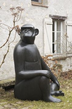 a statue of a monkey sitting on the ground next to a building with a window