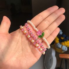 a person's hand holding three rings with pearls and flowers on them, all in different colors