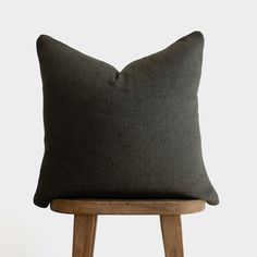 a dark gray pillow sitting on top of a wooden stool next to a white wall