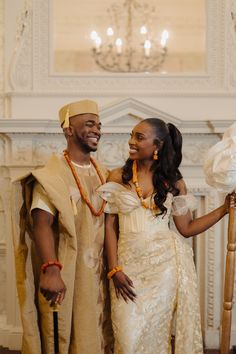 a man and woman standing next to each other in front of a fire place wearing traditional african garb