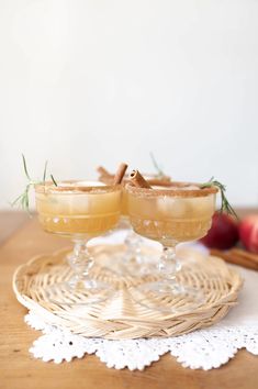 two glasses filled with apple cider on top of a wooden table next to apples