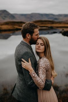 a man and woman embracing each other in front of a body of water with mountains in the background