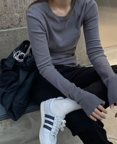 a woman sitting on the ground with her hand in her pocket and wearing white sneakers