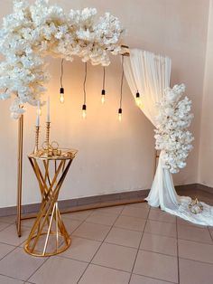 a white and gold wedding setup with flowers on the table, lights hanging from the ceiling