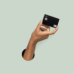 a person's hand holding up a black credit card against a gray background,