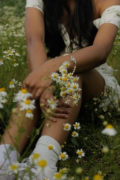 a woman sitting in the grass with daisies