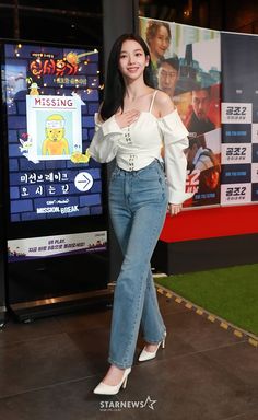 a woman standing in front of a movie poster wearing high waist jeans and white heels