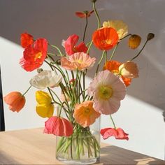 a vase filled with lots of colorful flowers on top of a wooden table next to a window