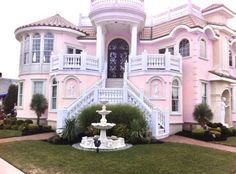 a pink and white house with a fountain in the front yard