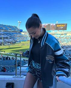 a woman in short shorts stands on the bleachers at a football game, looking down