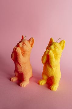 two small yellow and orange figurines sitting next to each other on a pink background