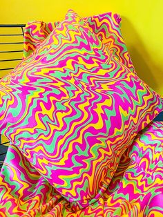 a bed with colorful sheets and pillows on top of it next to a yellow wall