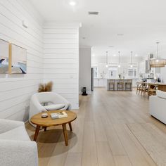 a living room filled with furniture next to a white kitchen and dining room table on top of a hard wood floor