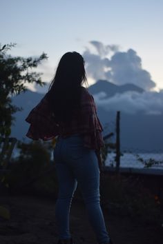 a woman standing in the dark with her back turned to the camera and clouds behind her