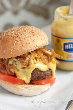 a cheeseburger with onions and tomato on a bun next to a jar of mustard