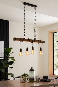 a dining room table with four lights hanging from it's center beam and two vases on the side