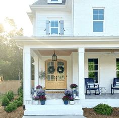 a white house with blue chairs and flowers on the front porch