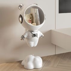 a small white space suit with a teddy bear in it's mouth and some books on the shelf