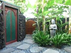 a small garden with a statue in the center and plants around it, along with a green door