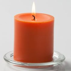 an orange candle is sitting on a glass plate