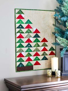 a christmas tree quilt hanging on the wall next to a lit candle and a small evergreen