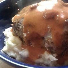 a blue bowl filled with meat and gravy covered in gravy on top of mashed potatoes