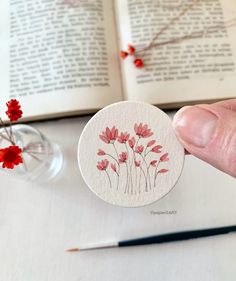 a hand holding a sticker with red flowers on it next to an open book