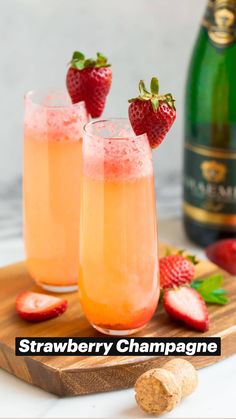 two glasses filled with champagne and strawberries on a cutting board next to a bottle