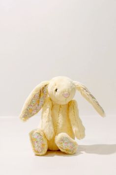 a white stuffed rabbit sitting in front of a white wall with glittered ears and tail