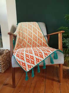 an orange and white blanket sitting on top of a chair next to a potted plant