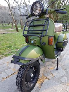 a green scooter parked on the sidewalk in front of some grass and trees