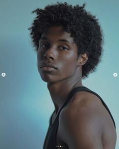 a man with an afro standing in front of a blue wall and looking at the camera